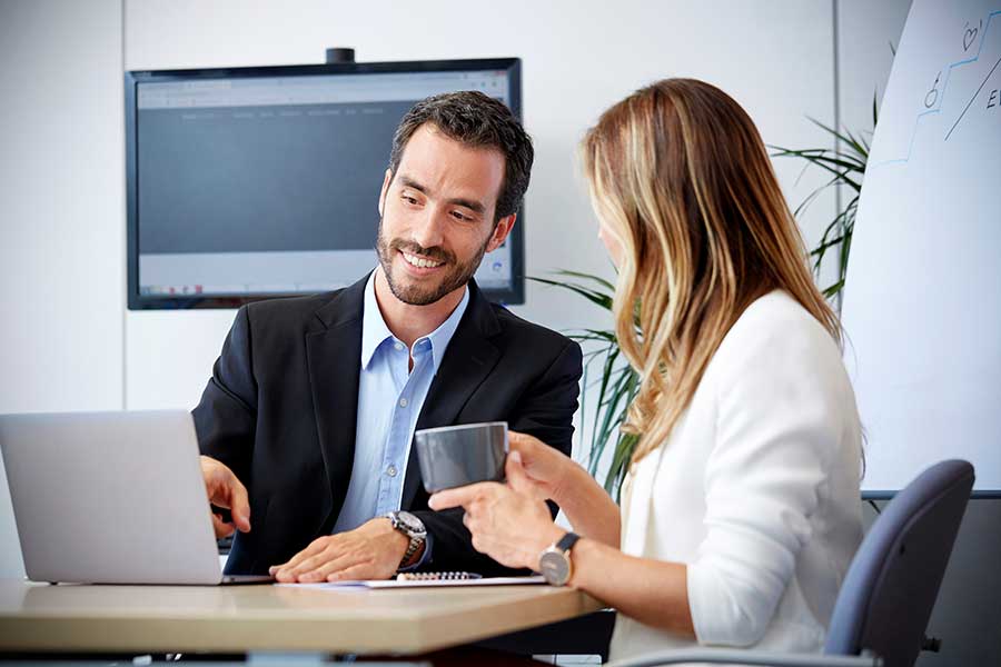 A Spanish translator smiling while pointing to his computer and talking with the client