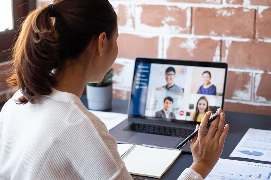 Woman waving to a team on a zoom call at her desk. 